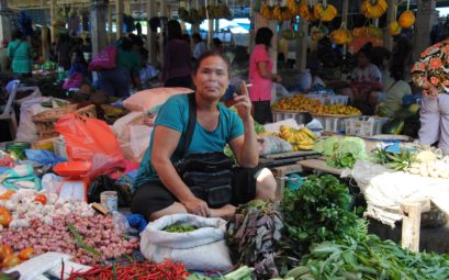 Eine rauchende Frau sitzt zwischen Gemüse auf dem Wochenmarkt