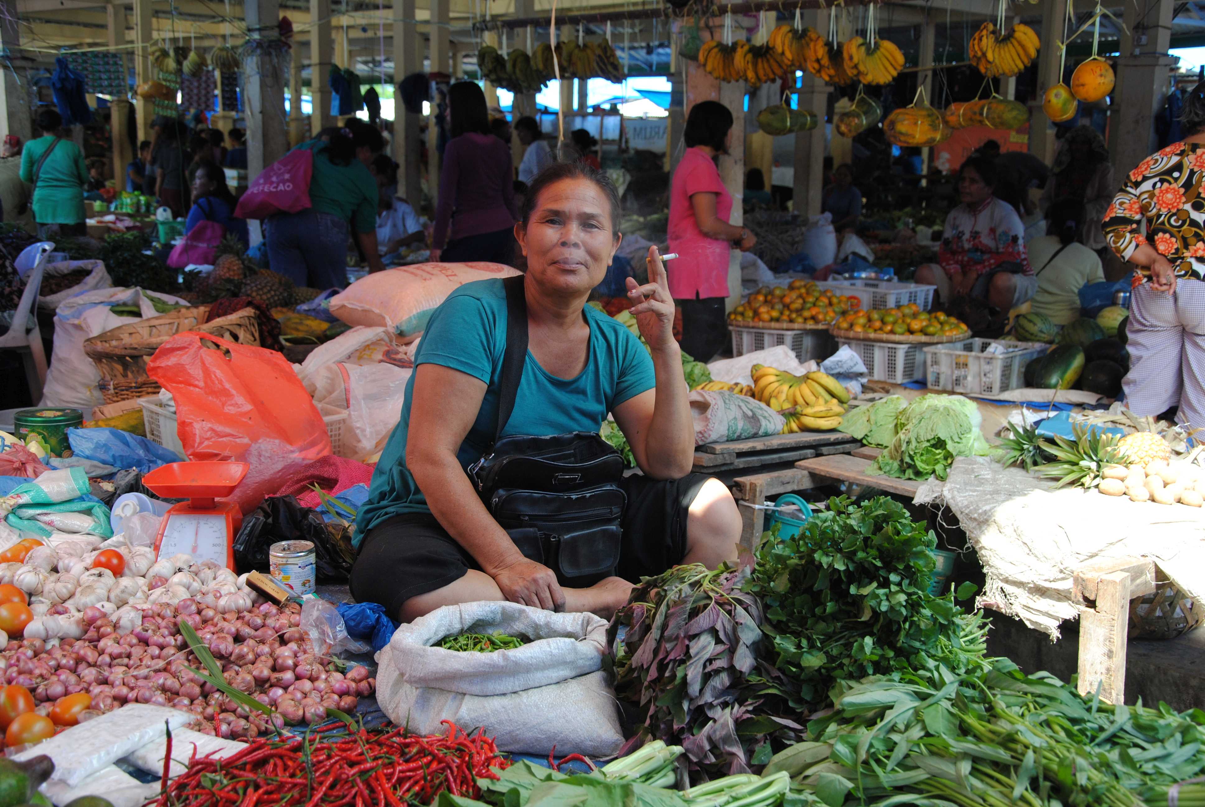 Eine Marktfrau sitzt rauchend auf ihrem Gemüsestand