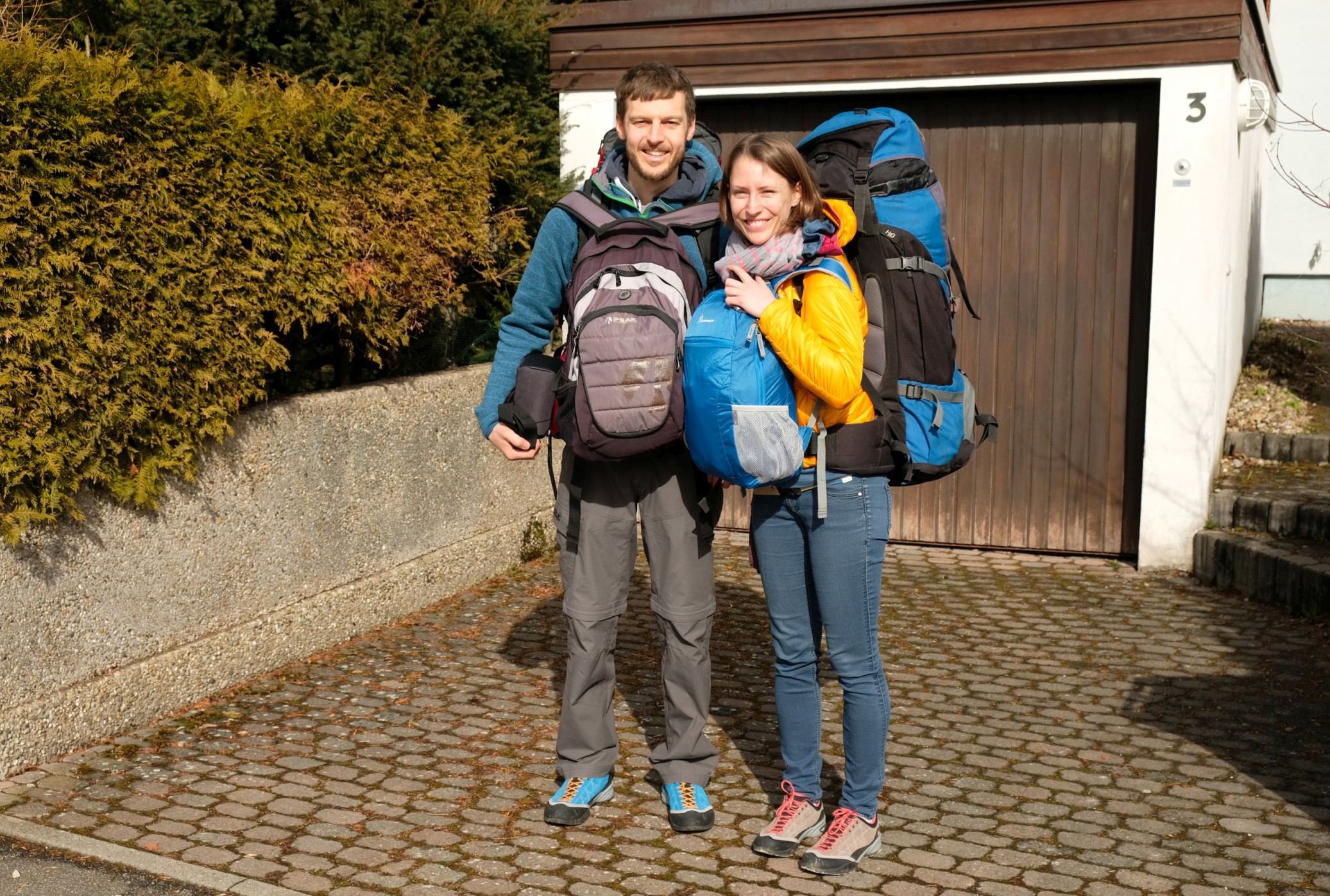 Sebastian und Leo stehen mit ihren Rucksäcken bepackt vor einer Garage