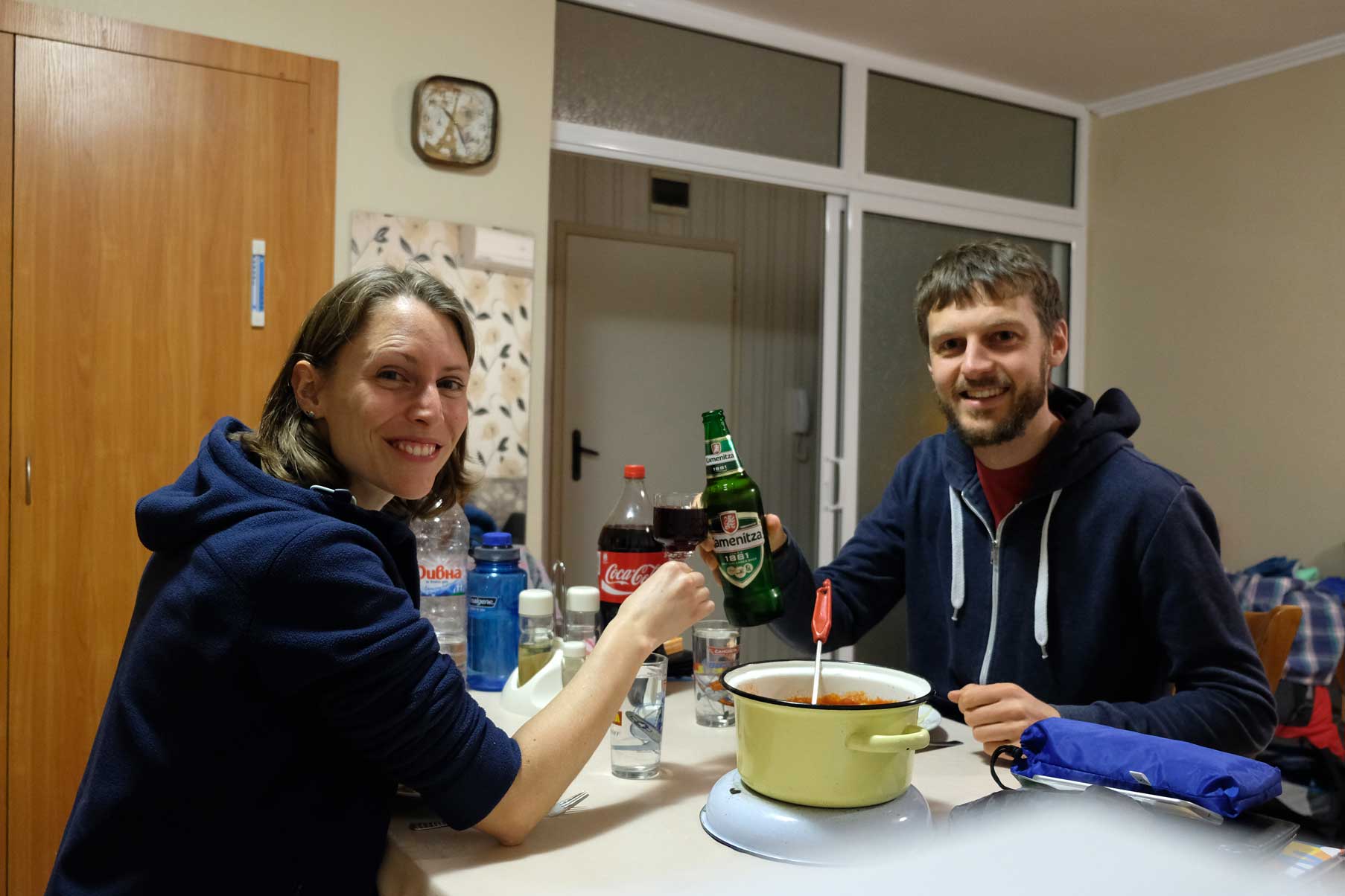 Leo und Sebastian sitzen am Tisch und stoßen mit Wein und Bier an