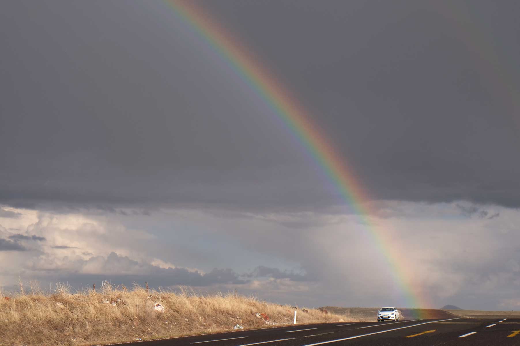 Ein Regenbogen vor dunklen Wolken trifft auf eine Straße