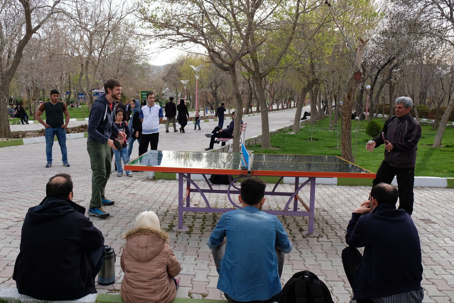 Sebastian spielt im Elgoli-Park mit einem Mann Tischtennis. Einige Leute beobachten das Match.