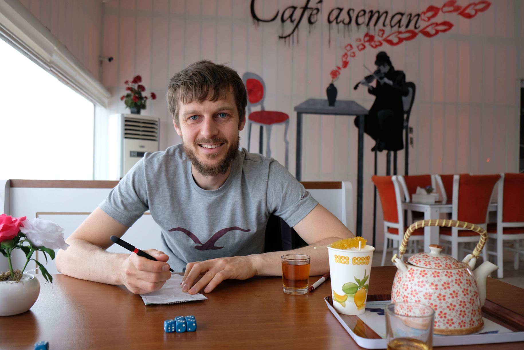 Sebastian sitzt mit Spielwürfeln und einer Tasse Tee an einem Tisch