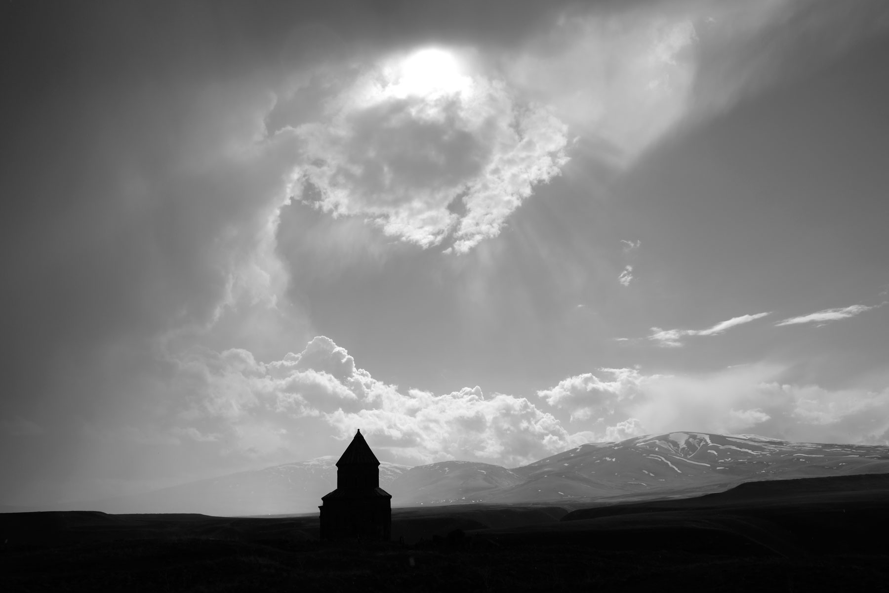 Silhouette des Schamatun der Apostelkirche. Die Sonne kommt hinter den Wolken hervor.