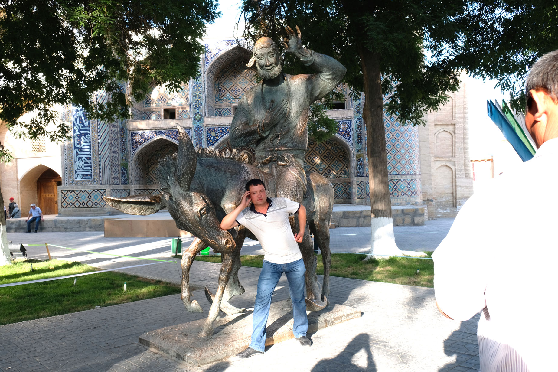 Ein Mann posiert vor einer Bronzestatue, die einen Esel und einen Reiter zeigt