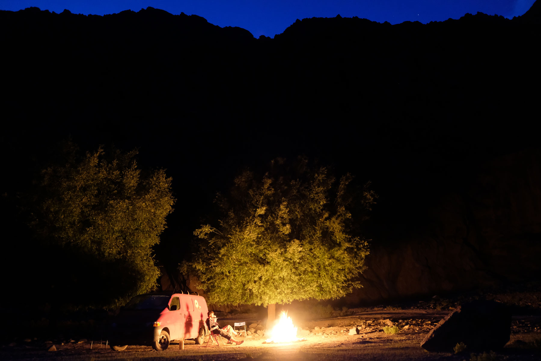 Ein roter Kleintransporter steht neben einem Lagerfeuer