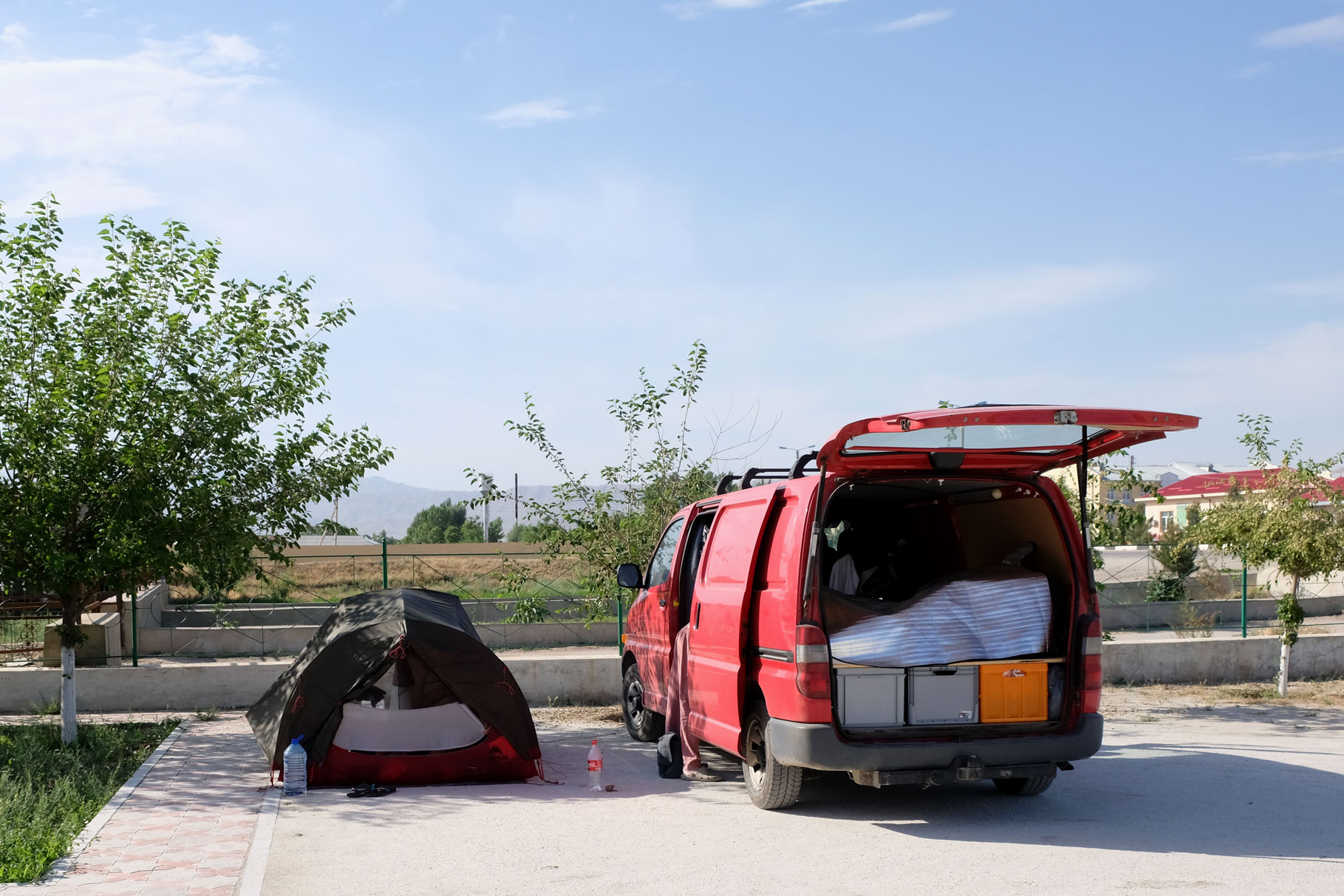 Ein Zelt steht neben einem roten Kleintransporter auf einem Parkplatz