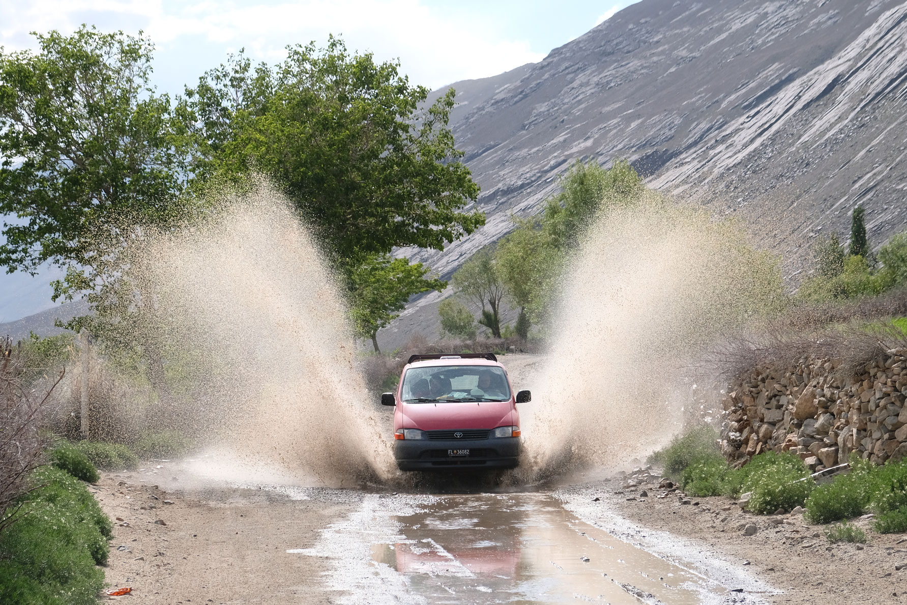 Ein roter Kleintransporter fährt durch eine Pfütze auf dem Pamir Highway.