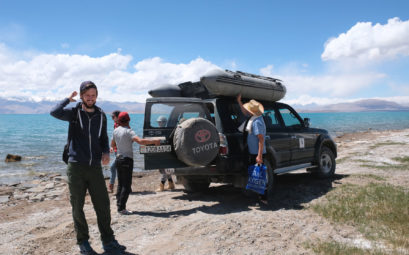 Sebastian am Karakul See vor einem Geländewagen, auf dessen Dach ein Schlauchboot ist.