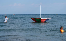 Ein Mann watet im Issyk-Kul See und versucht, einen davonschwimmenden Sonnenschirm einzufangen.