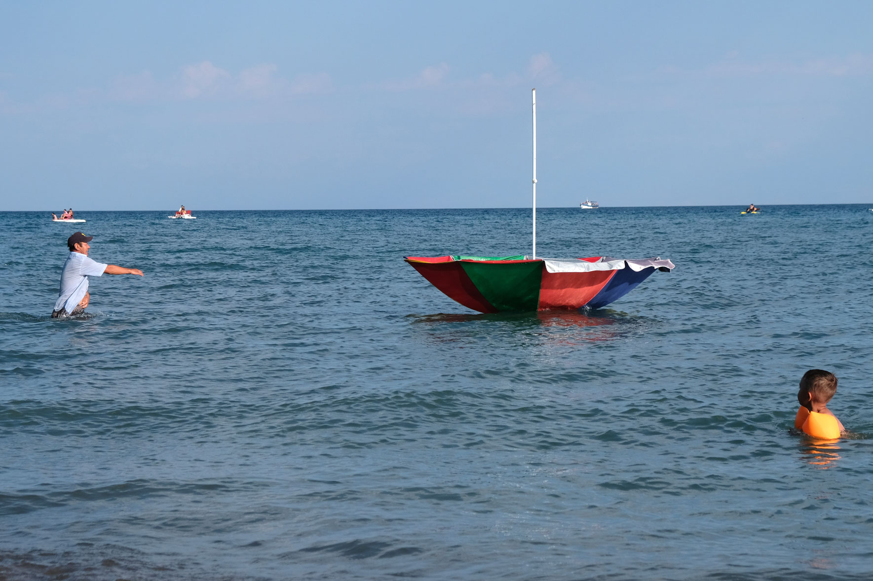 Ein Mann watet im Issyk-Kul See und versucht, einen davonschwimmenden Sonnenschirm einzufangen.