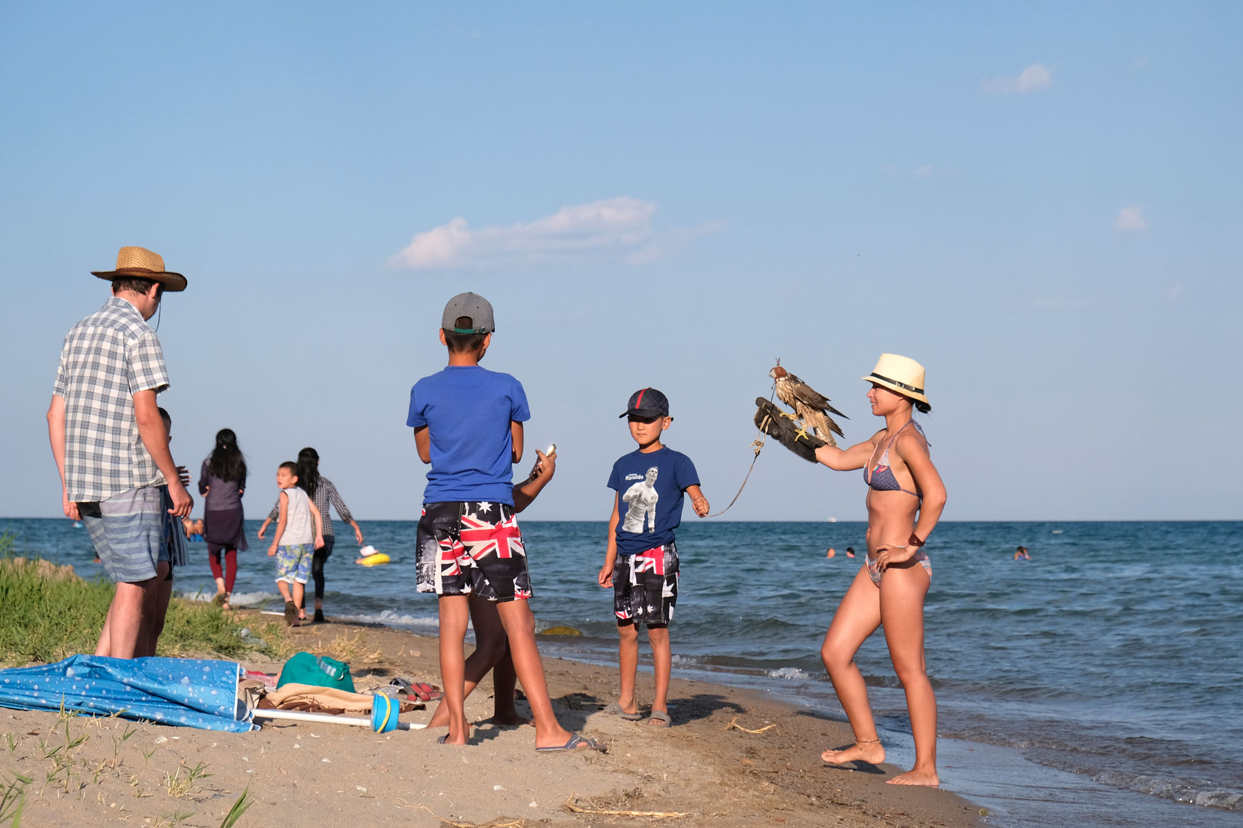 Eine Frau in Bikini hält am Uder des Issyk-Kul einen Falken auf dem Arm.