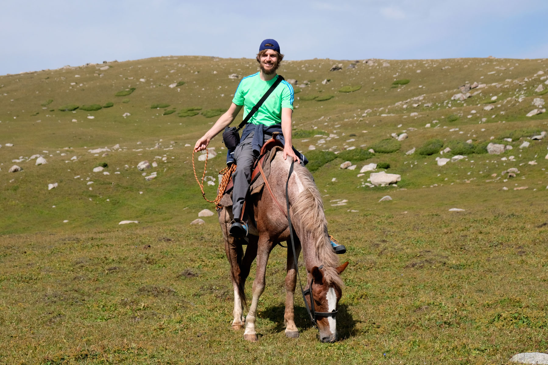 Sebastian sitzt auf einem Pferd, das Gras frisst.