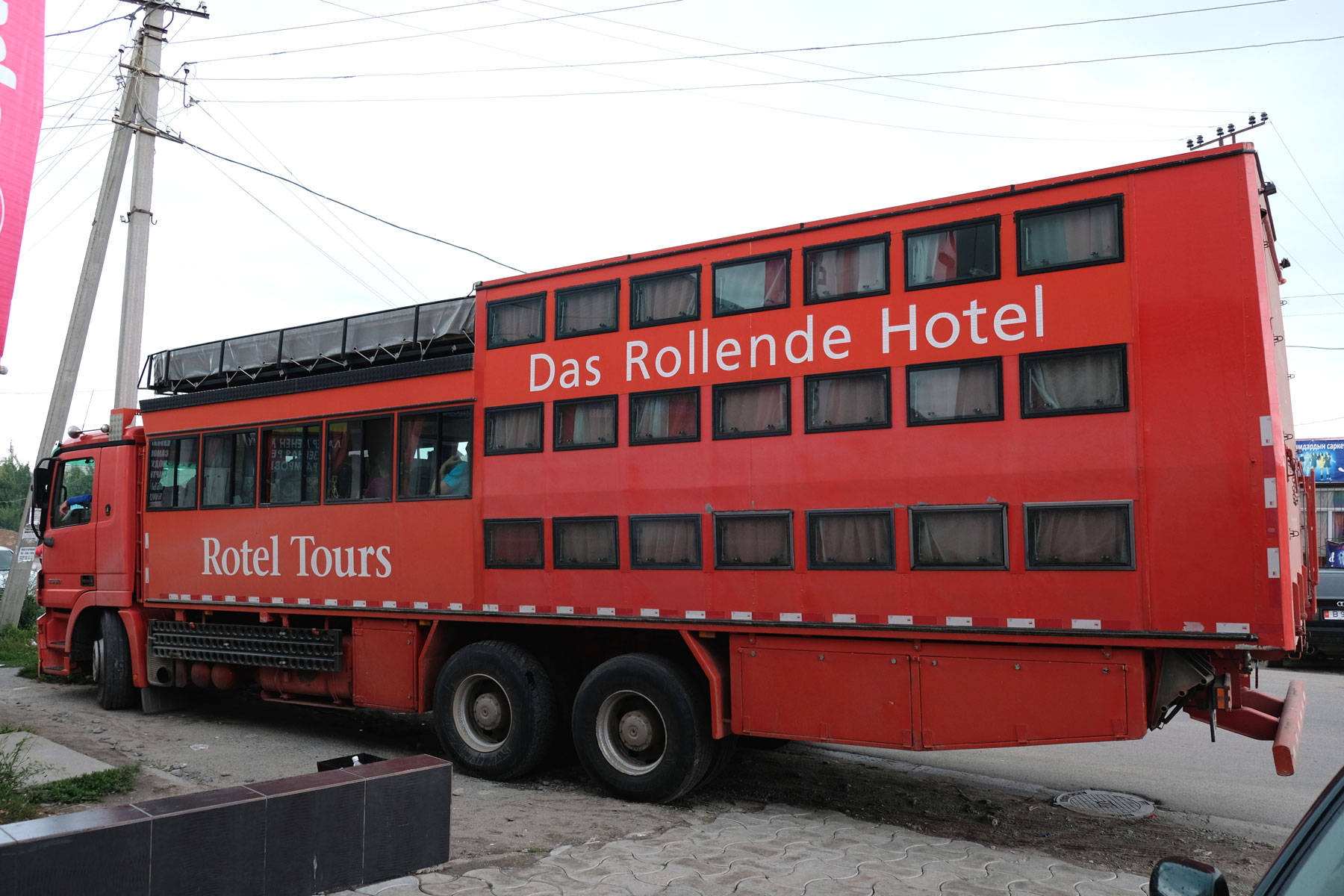 Ein großer roter Lastwagen mit vielen Fenstern, auf dem "Das Rollende Hotel" steht.