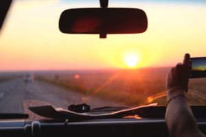 Jemand macht aus einem Auto heraus ein Handyfoto vom Sonnenuntergang.