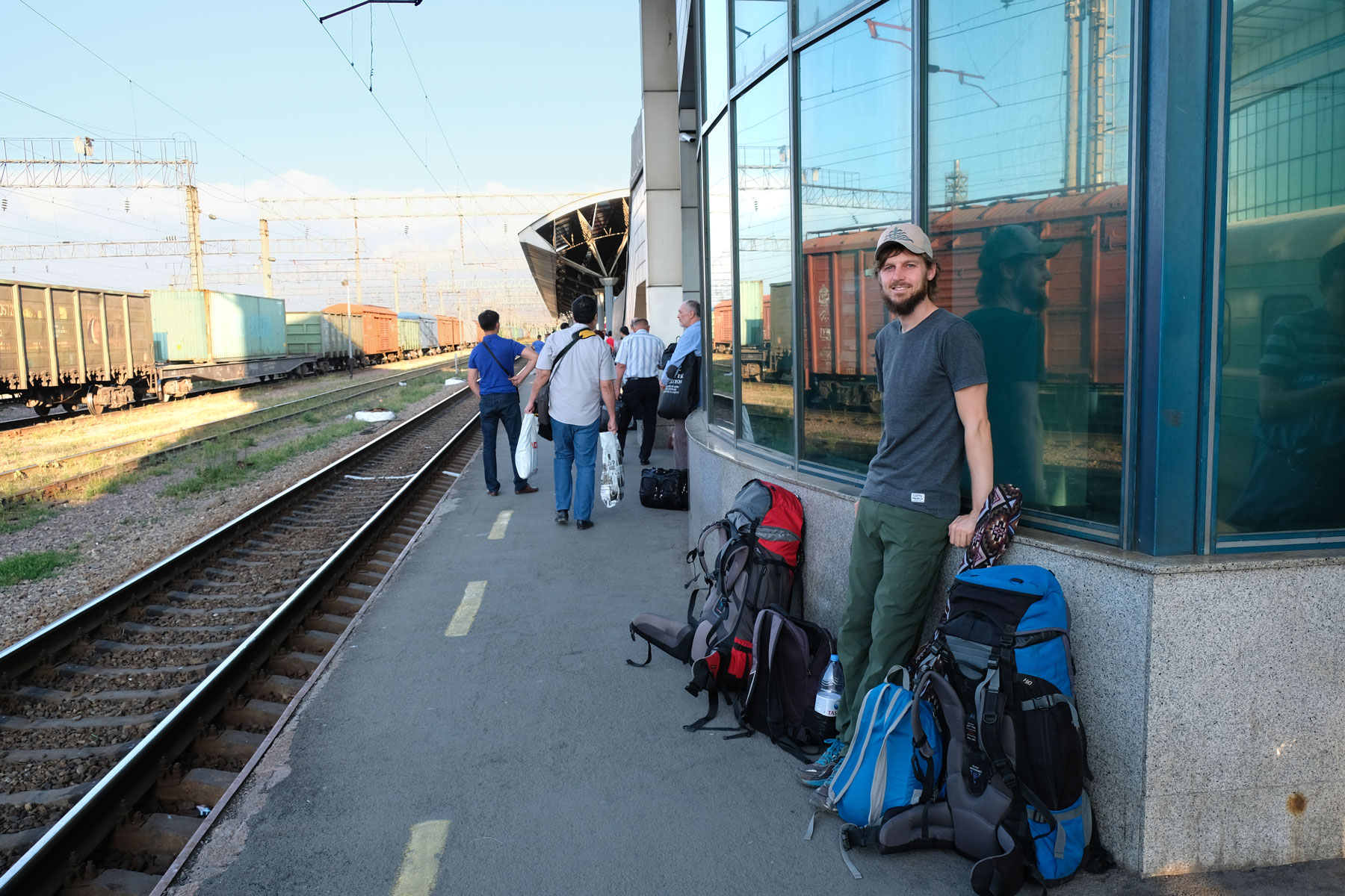 Sebastian steht neben Rucksäcken an einem Bahnsteig des Hauptbahnhofs von Almaty.