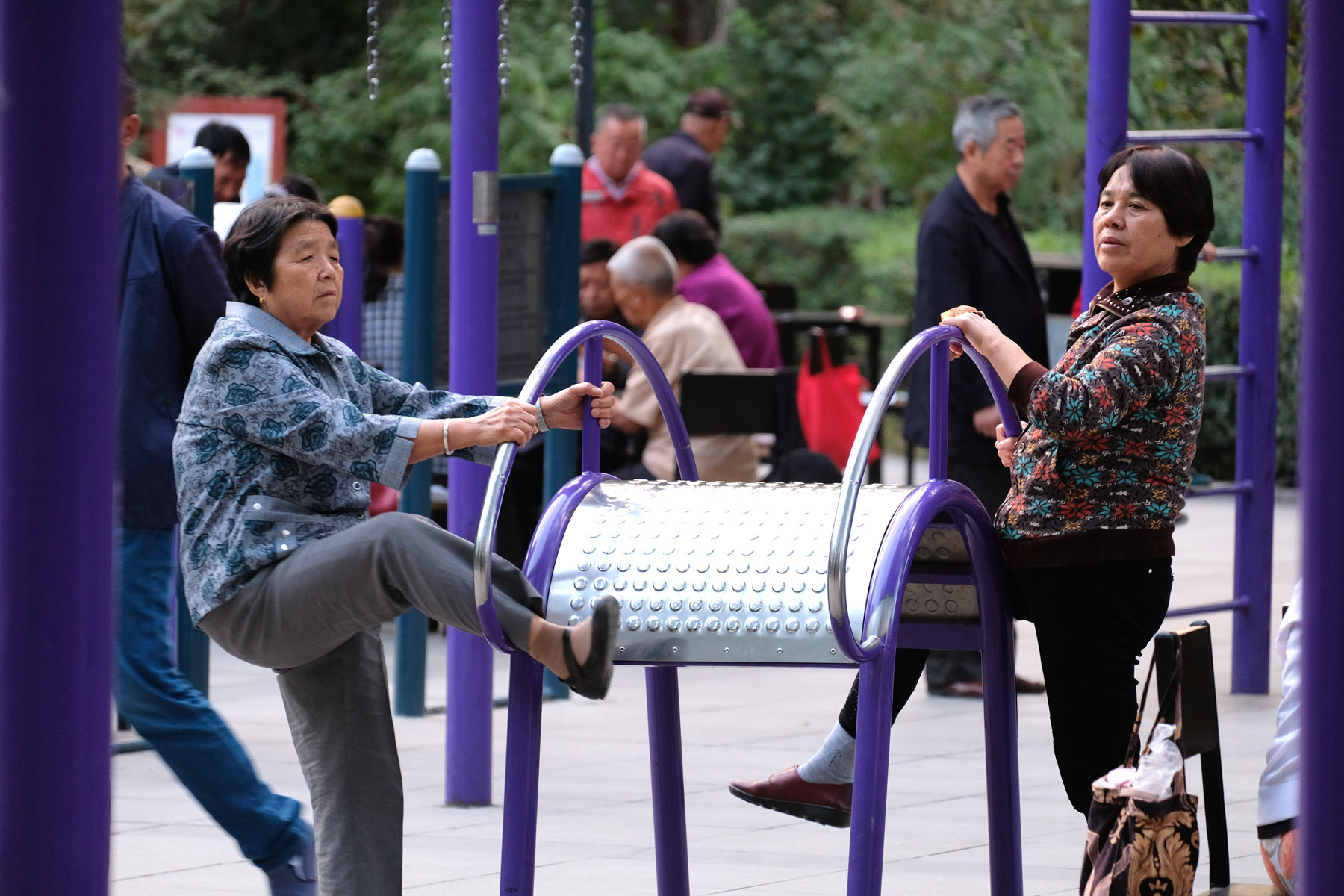 Zwei chinesische Frauen machen Leibesübungen an einem Sportgerät in einem Park.