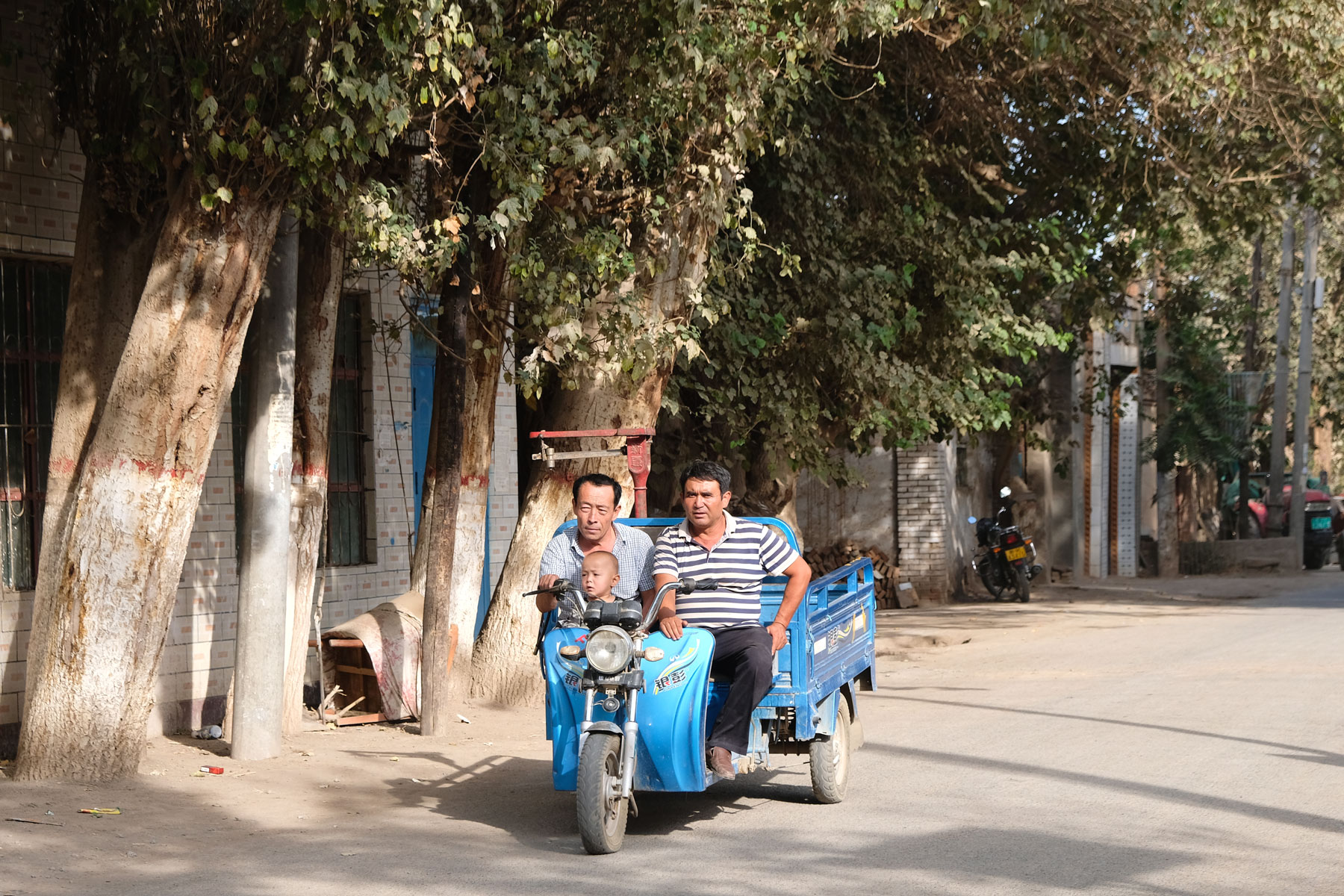 Zwei uigurische Männer und ein Junge fahren auf einem Trike.