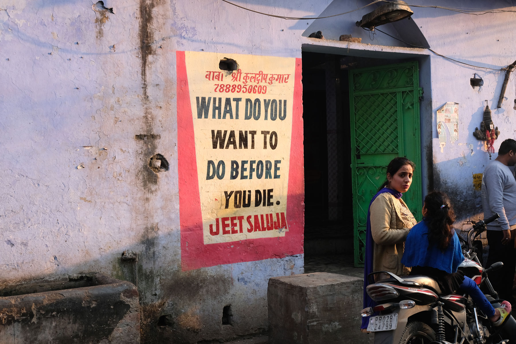 Eine indische Frau steht neben einem Schild, das die Frage stellt, was man noch machen möchte, bevor man stirbt.