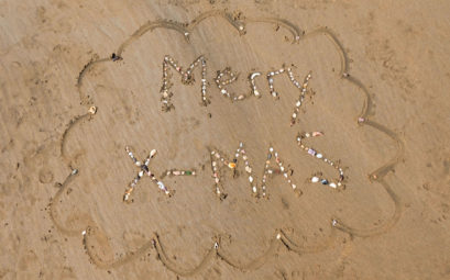 Die Worte "Merry X-Mas" mit Muscheln auf Sand gelegt.