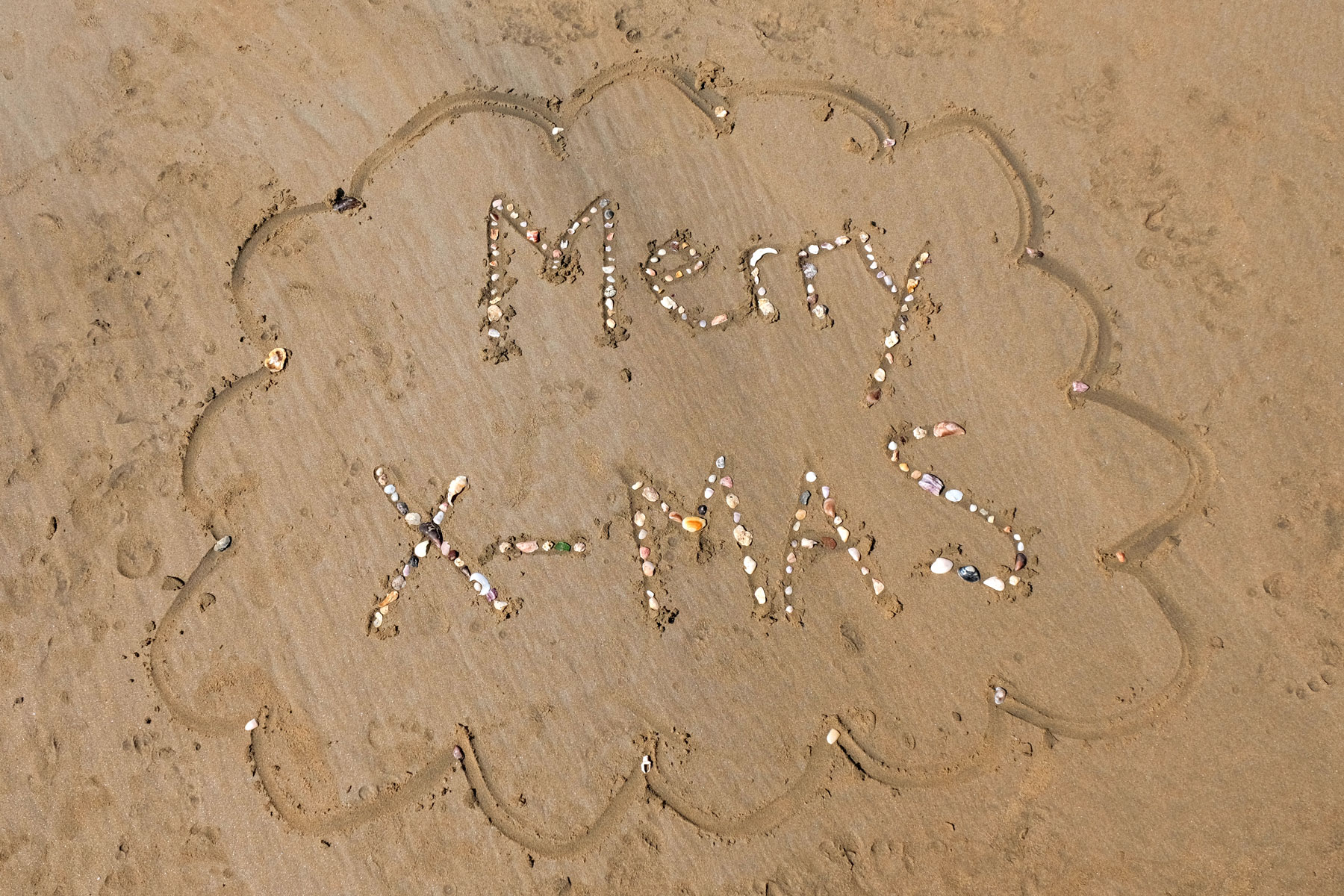 Die Worte "Merry X-Mas" mit Muscheln auf Sand gelegt.