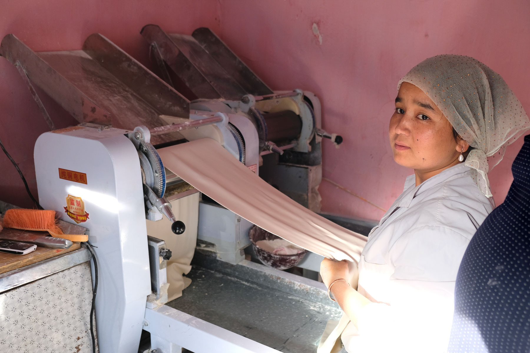Eine uigurische Frau rollt an einer Maschine Nudelteig aus.