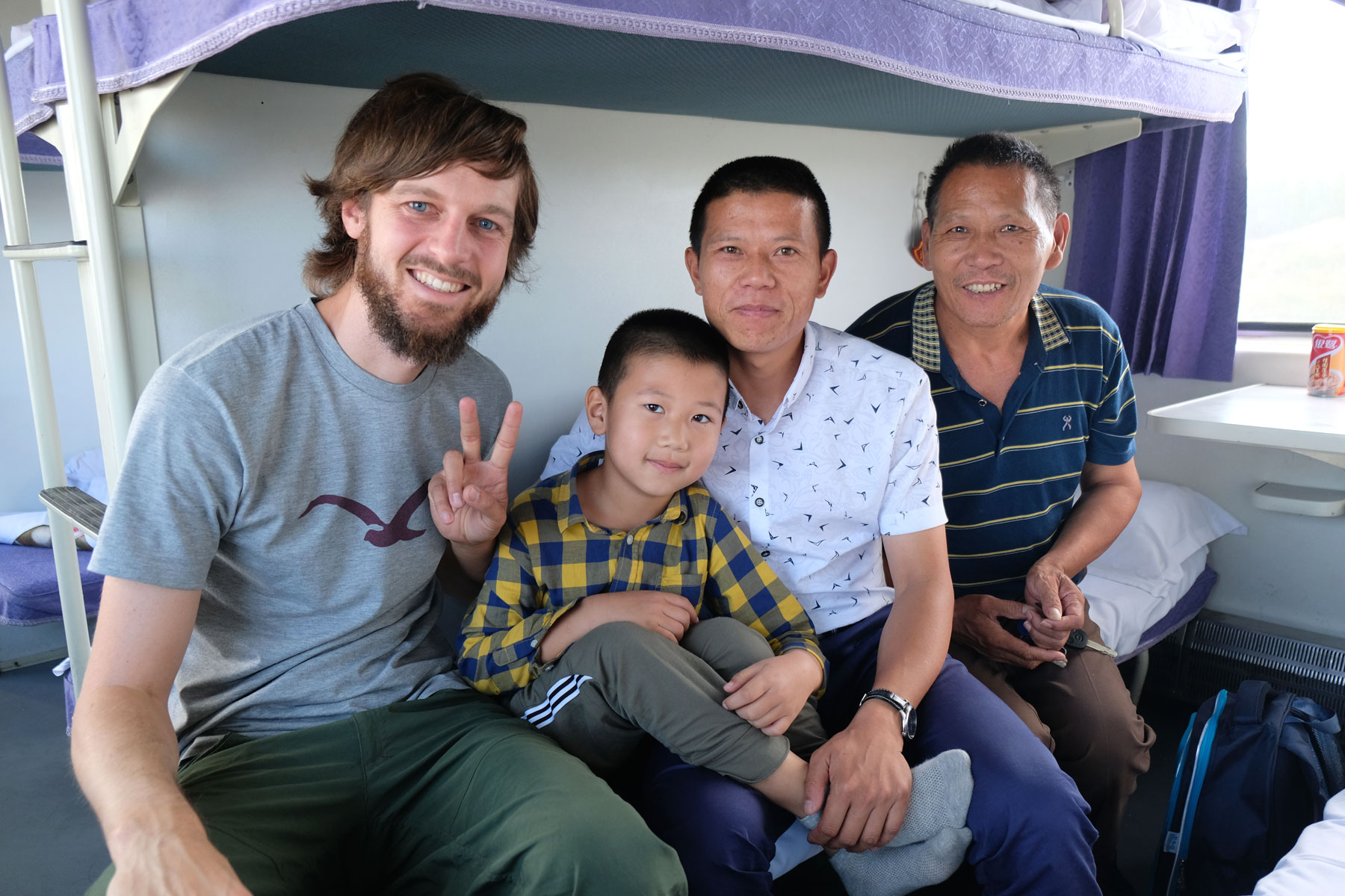 Sebastian sitzt mit zwei chinesischen Männern und einem Jungen auf dem Bett im Schlafwagen eines Zugs.