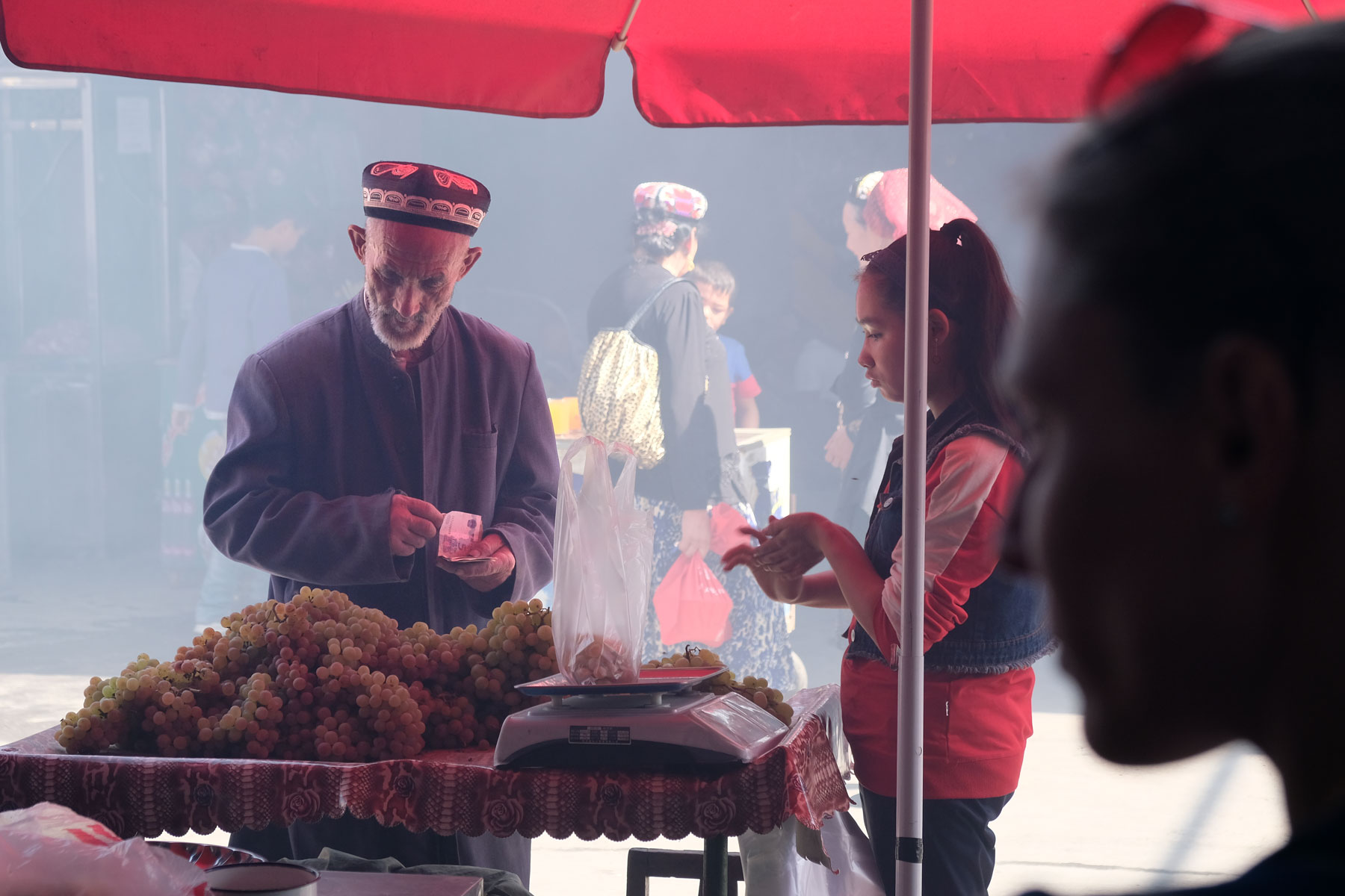 Ein alter Mann kauft Trauben an einem Marktstand in Hotan.