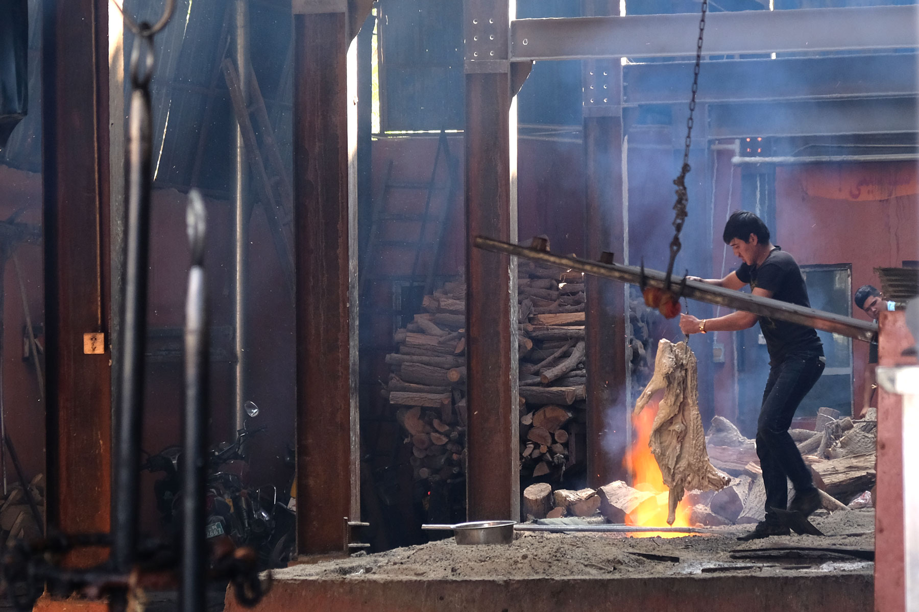 Ein Mann hält einen Haken über einem Feuer, an dem ein großes Stück Fleisch hängt.