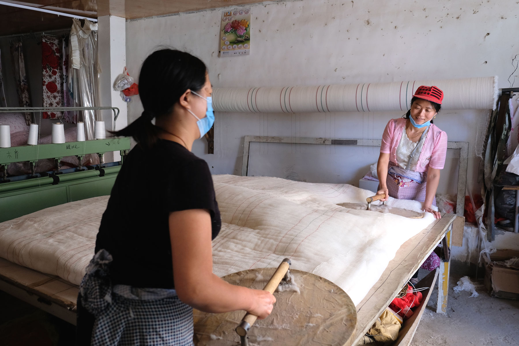 Zwei Arbeiterinnen pressen Baumwolle mit einem runden Werkzeug.