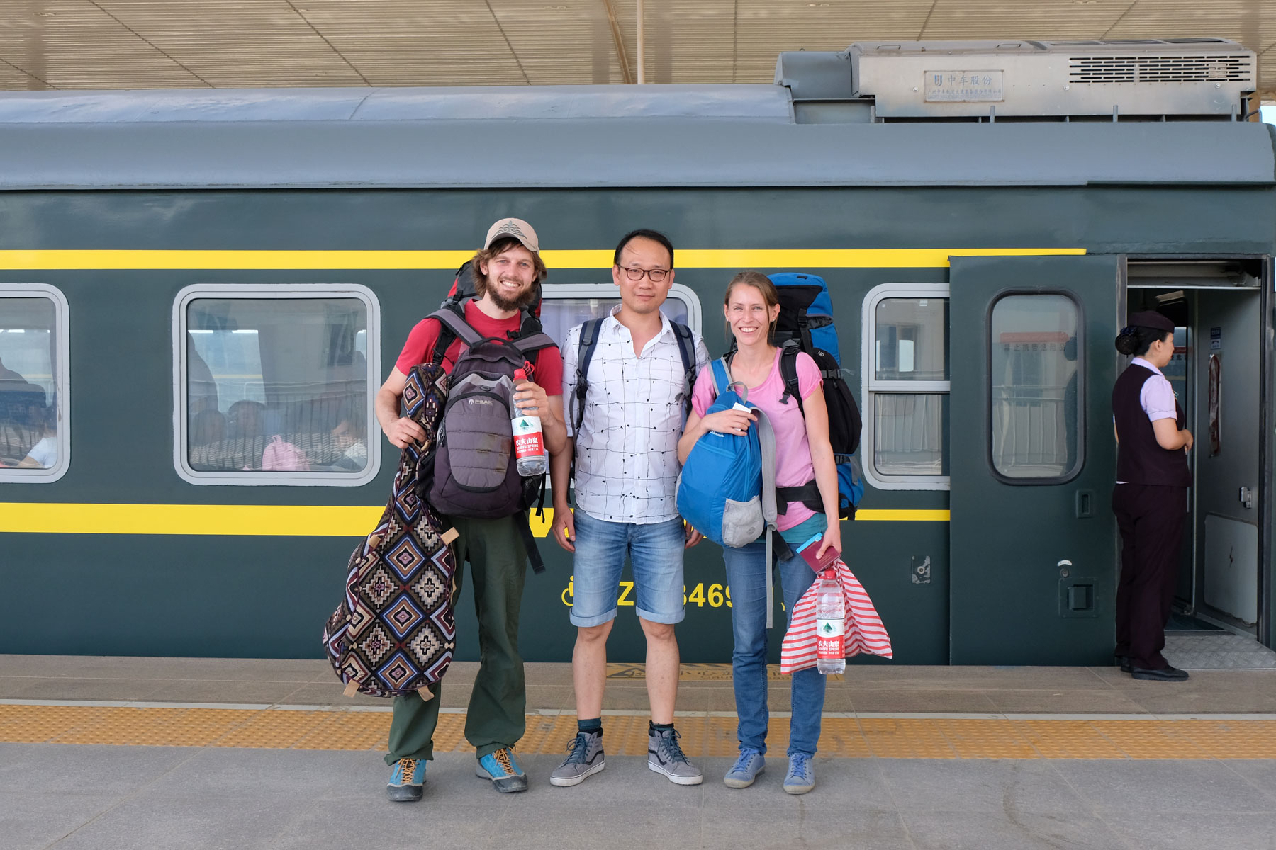 Sebastian und Leo stehen mit Gepäck neben einem Chinesen vor einem Zug am Bahnhof von Hotan.