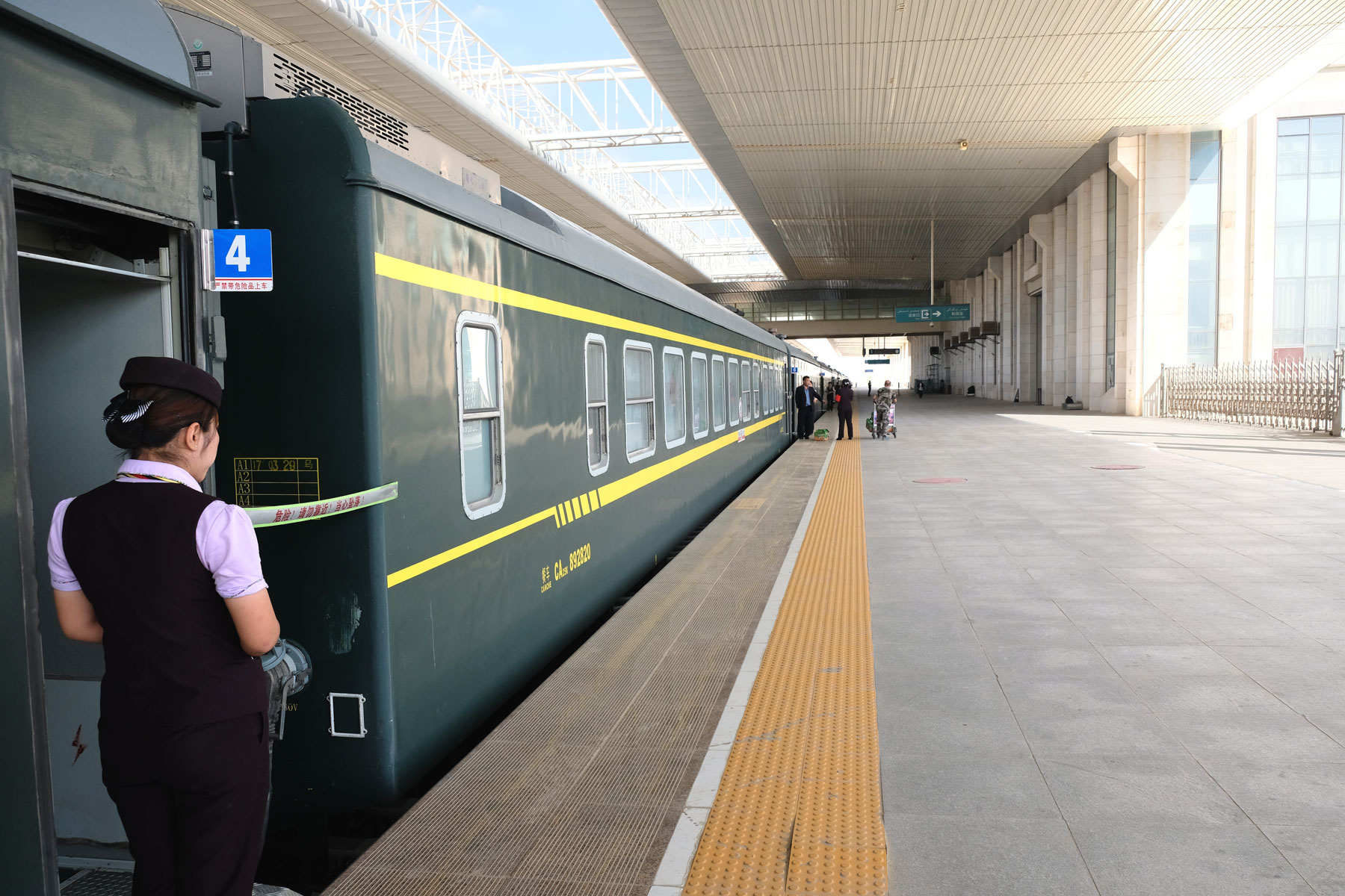 Eine Zugbegleiterin neben einem Zug am Bahnhof von Hotan.