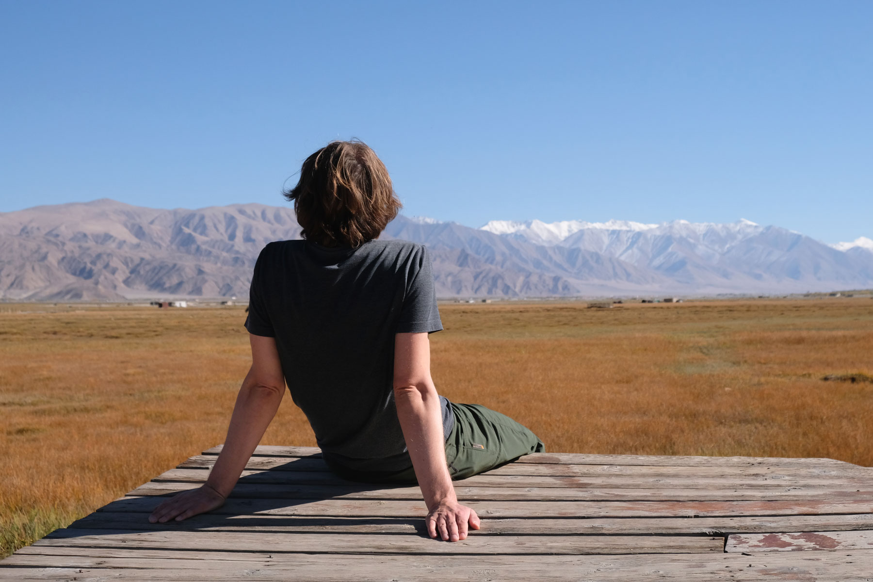 Sebastian sitzt auf einem Holzsteg in den Grasslands in Tashkurgan.