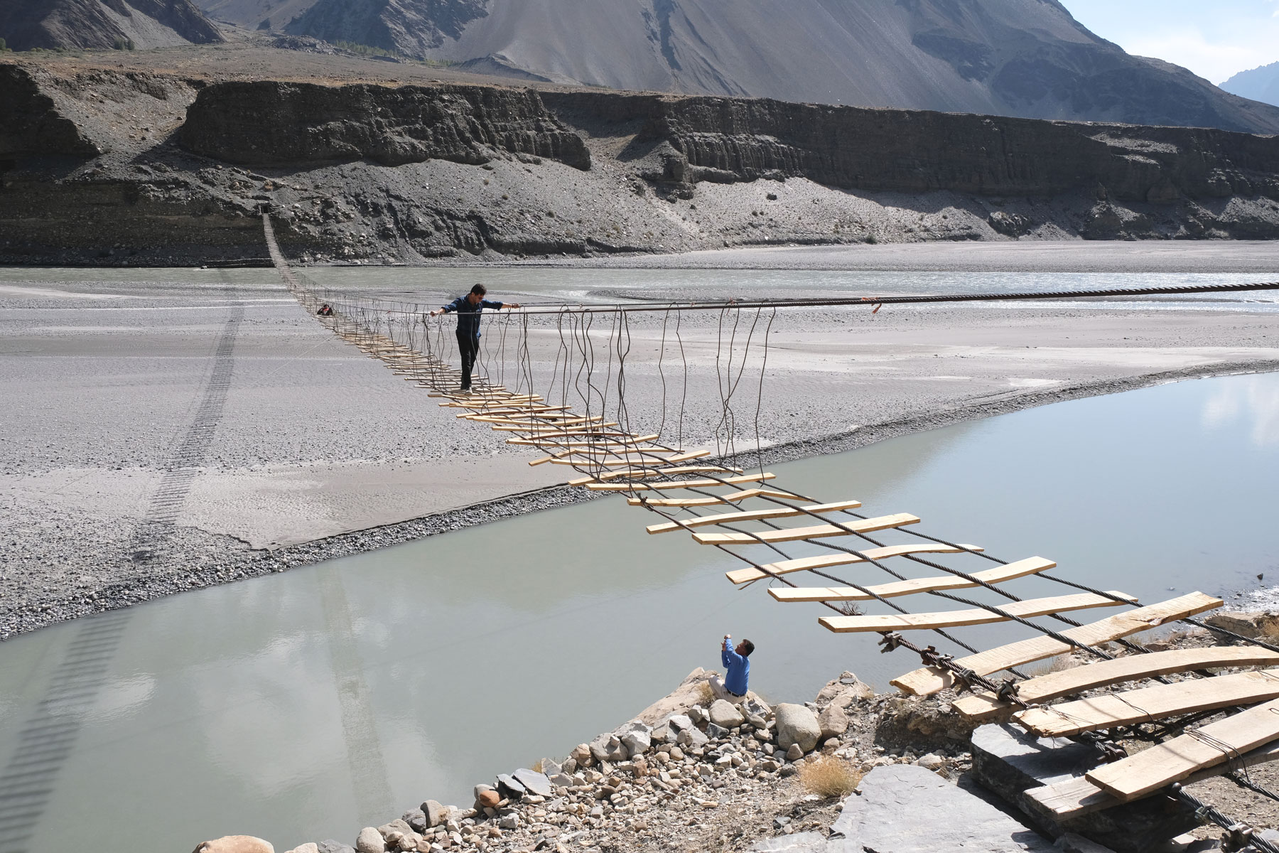 Ein Mann geht auf einer Hängebrücke über den Hunza-Fluss.