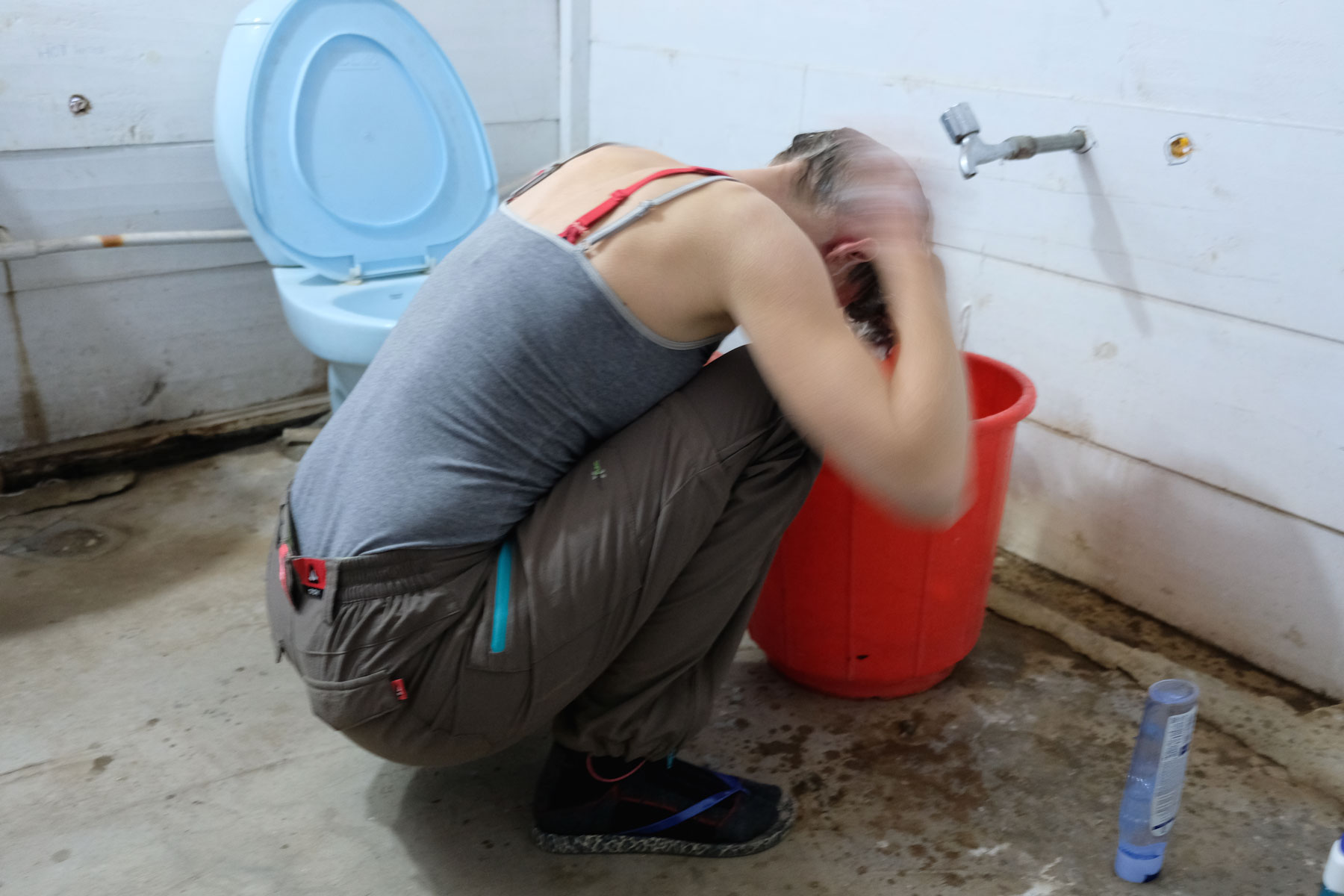 Leo wäscht sich über einem Eimer hockend die Haare.