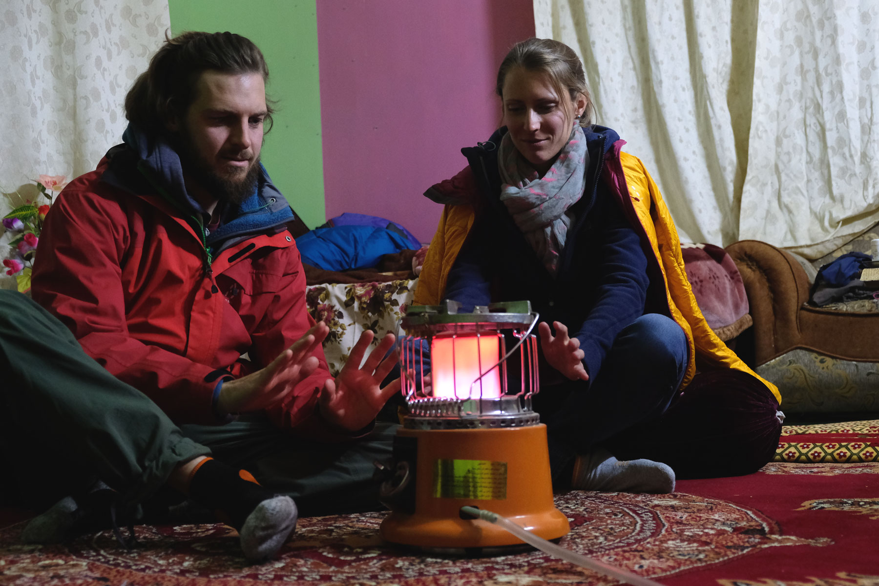 Sebastian und Leo sitzen in Jacken gehüllt um eine Gasheizung.