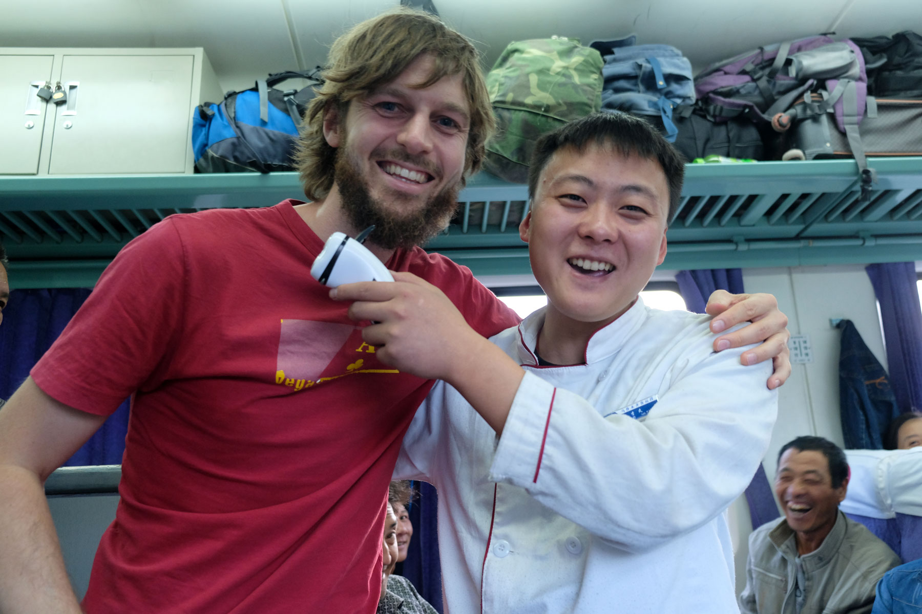 Sebastian steht neben einem chinesischen Verkäufer, der ihm einen Bartschneider an den Bart hält.