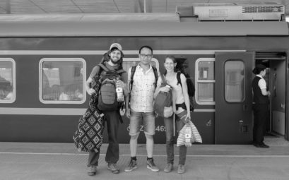 Sebastian und Leo stehen neben einem Chinesen vor einem Zug im Bahnhof von Hotan.