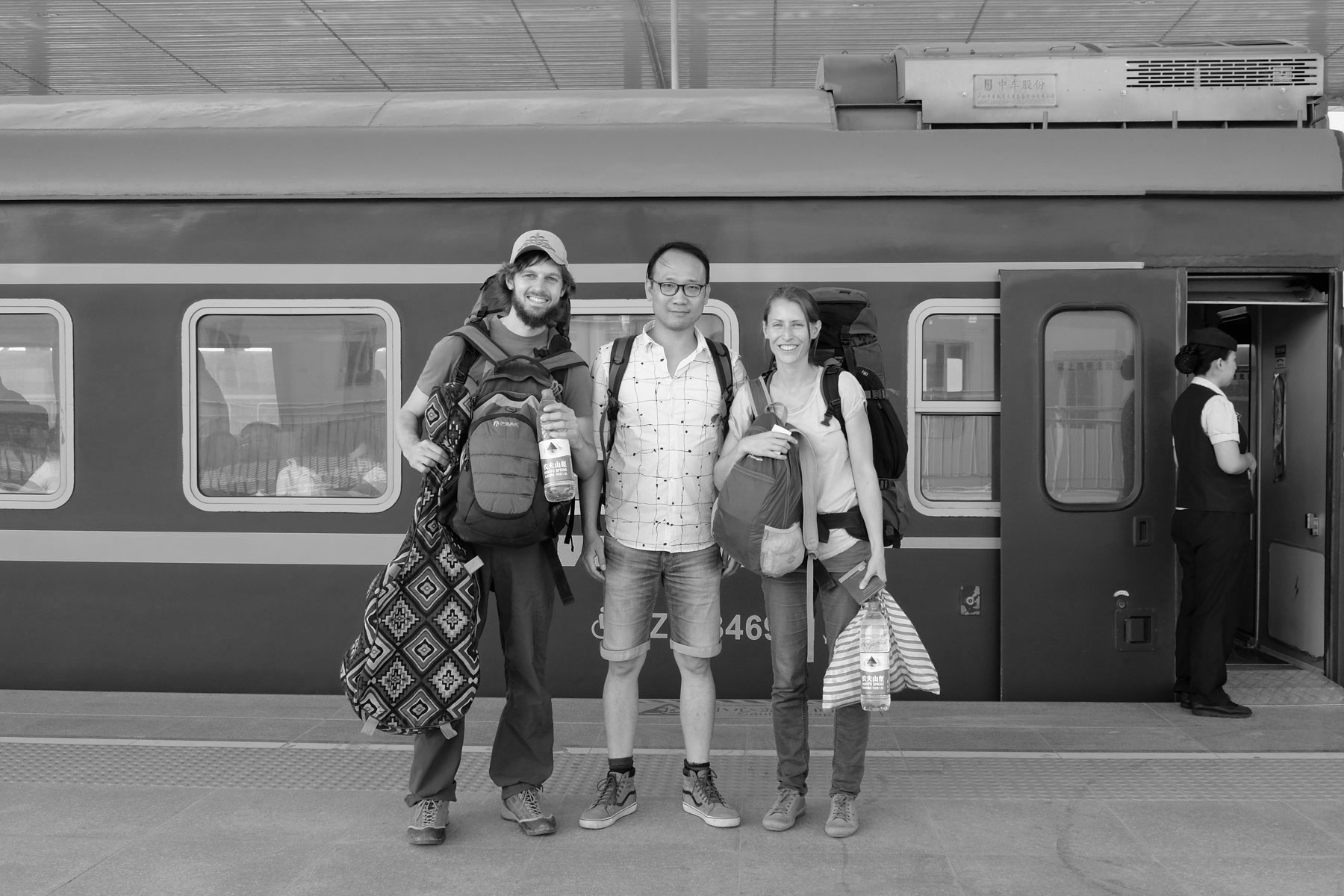 Sebastian und Leo stehen neben einem Chinesen vor einem Zug im Bahnhof von Hotan.