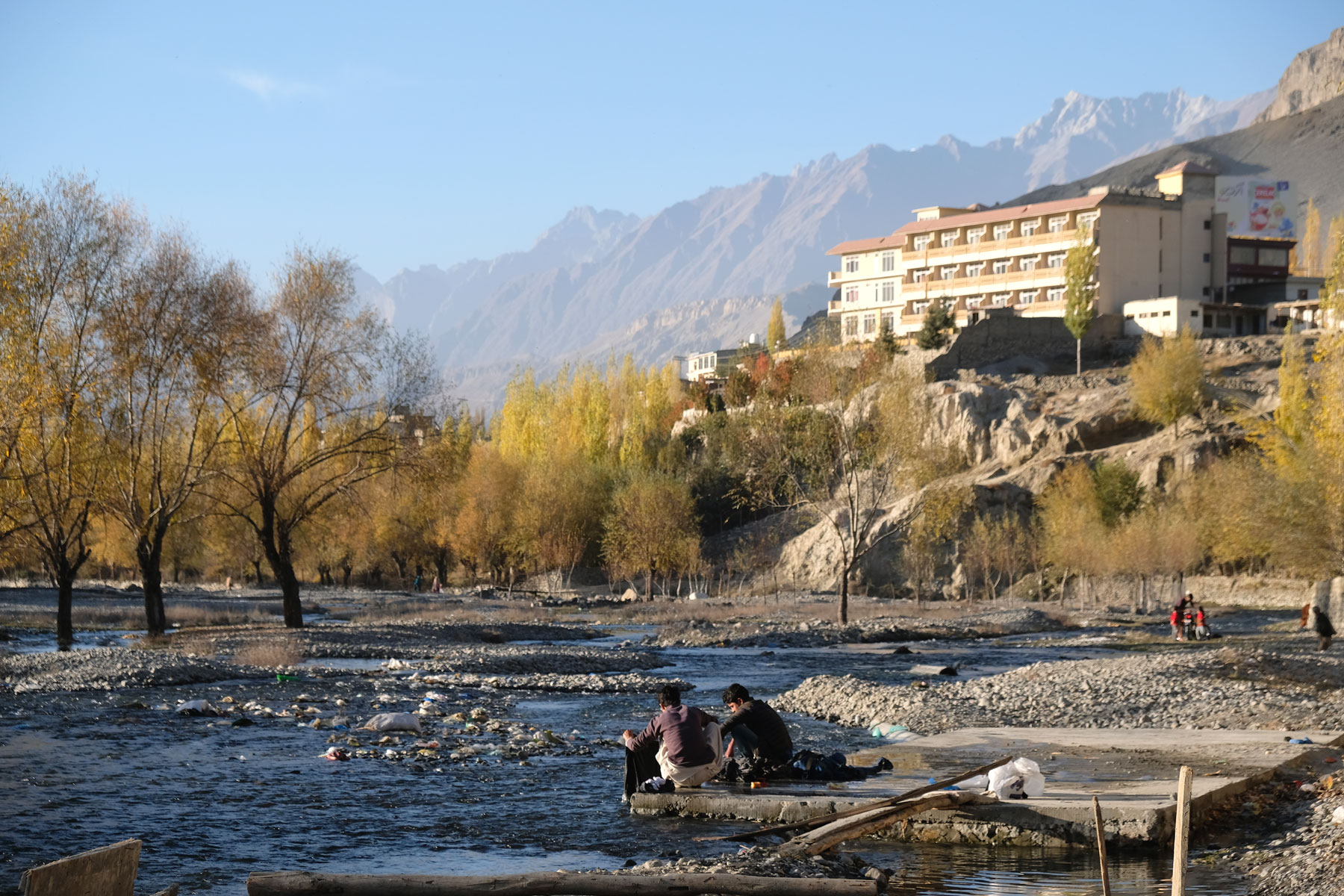 Zwei Jungen waschen in einem Fluss Wäsche. Ein Hotel in Skardu steht auf einem Felsen.