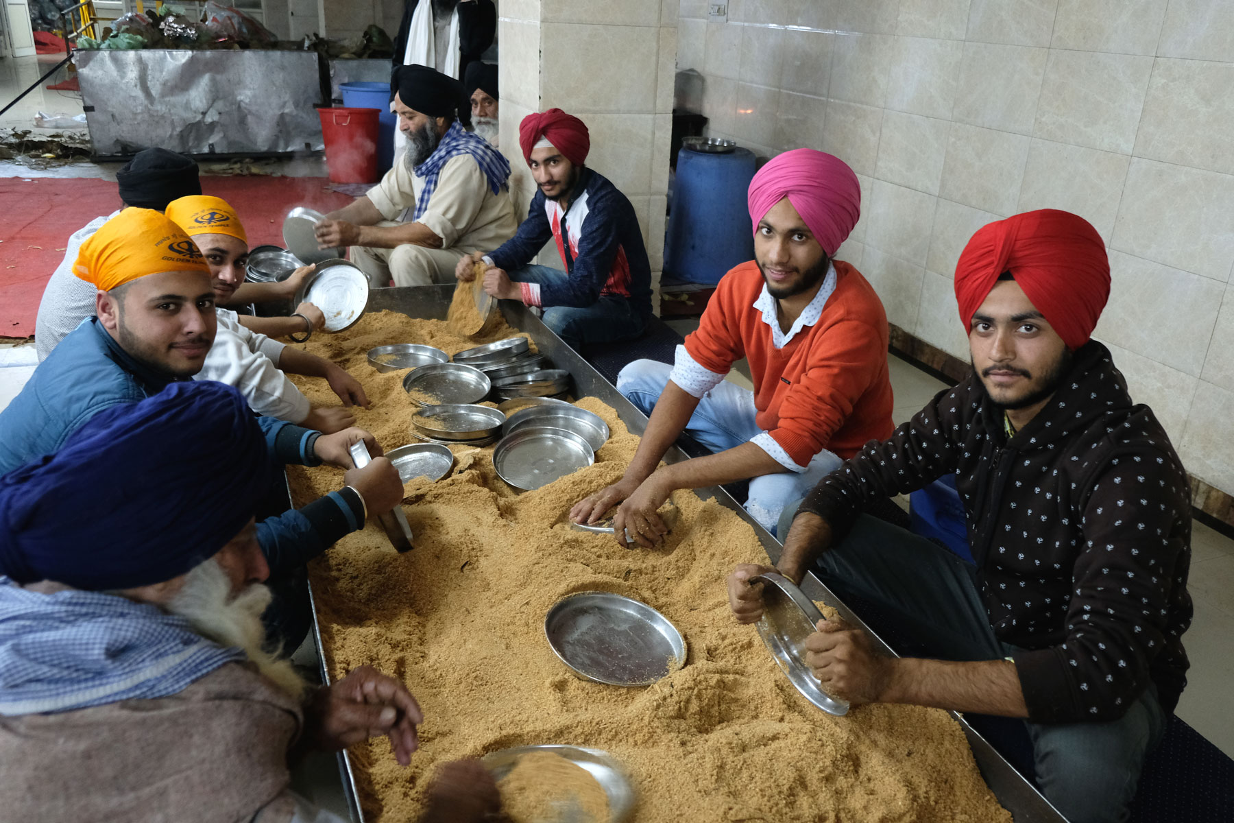 Indische Männer mit Turbanen waschen Teller in einer mit Sägespänen gefüllten Wanne.