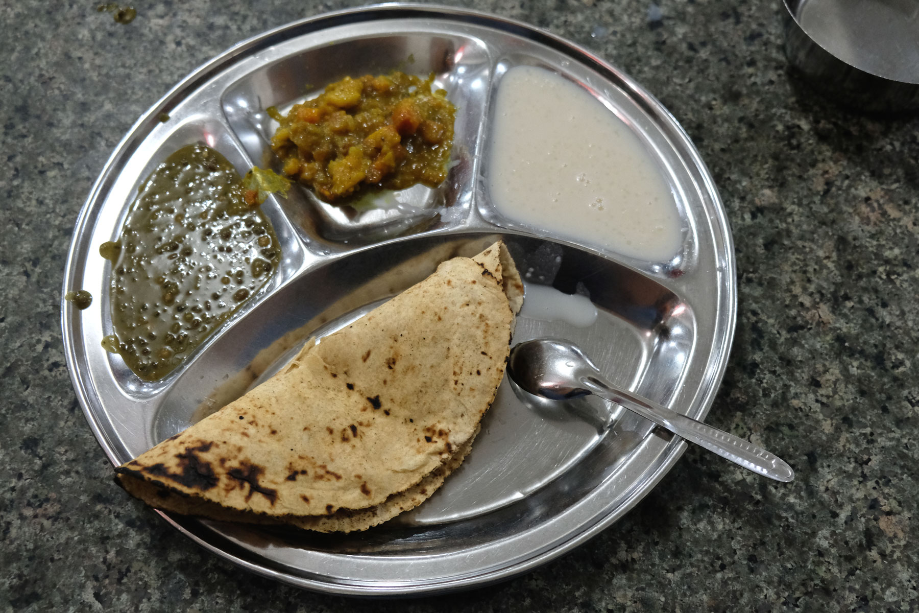 Linsen, Curry, Milchreis und Chapati auf einem Metallteller.