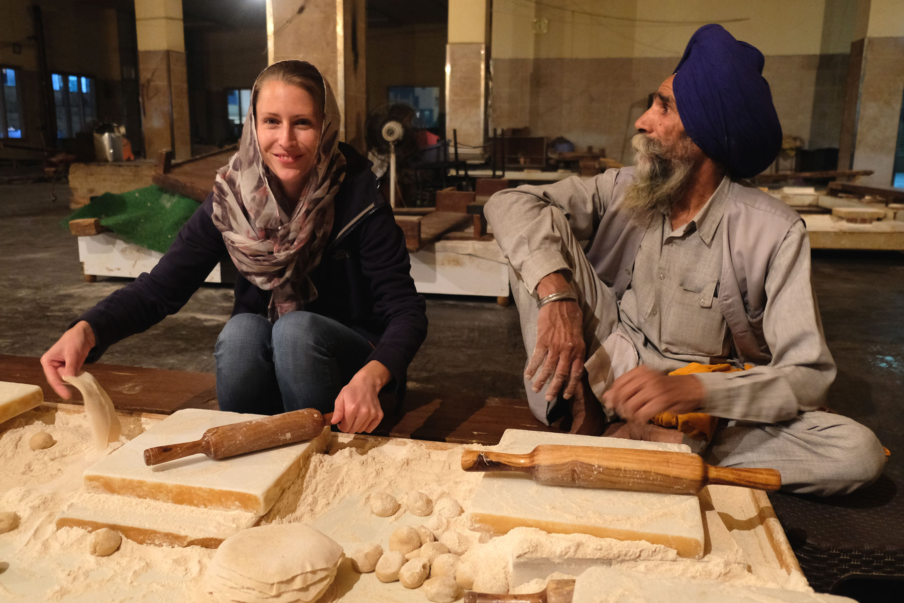 Leo sitzt neben einem alten Mann im goldenen Sikh-Tempel und rollt Teig für Chapati aus.