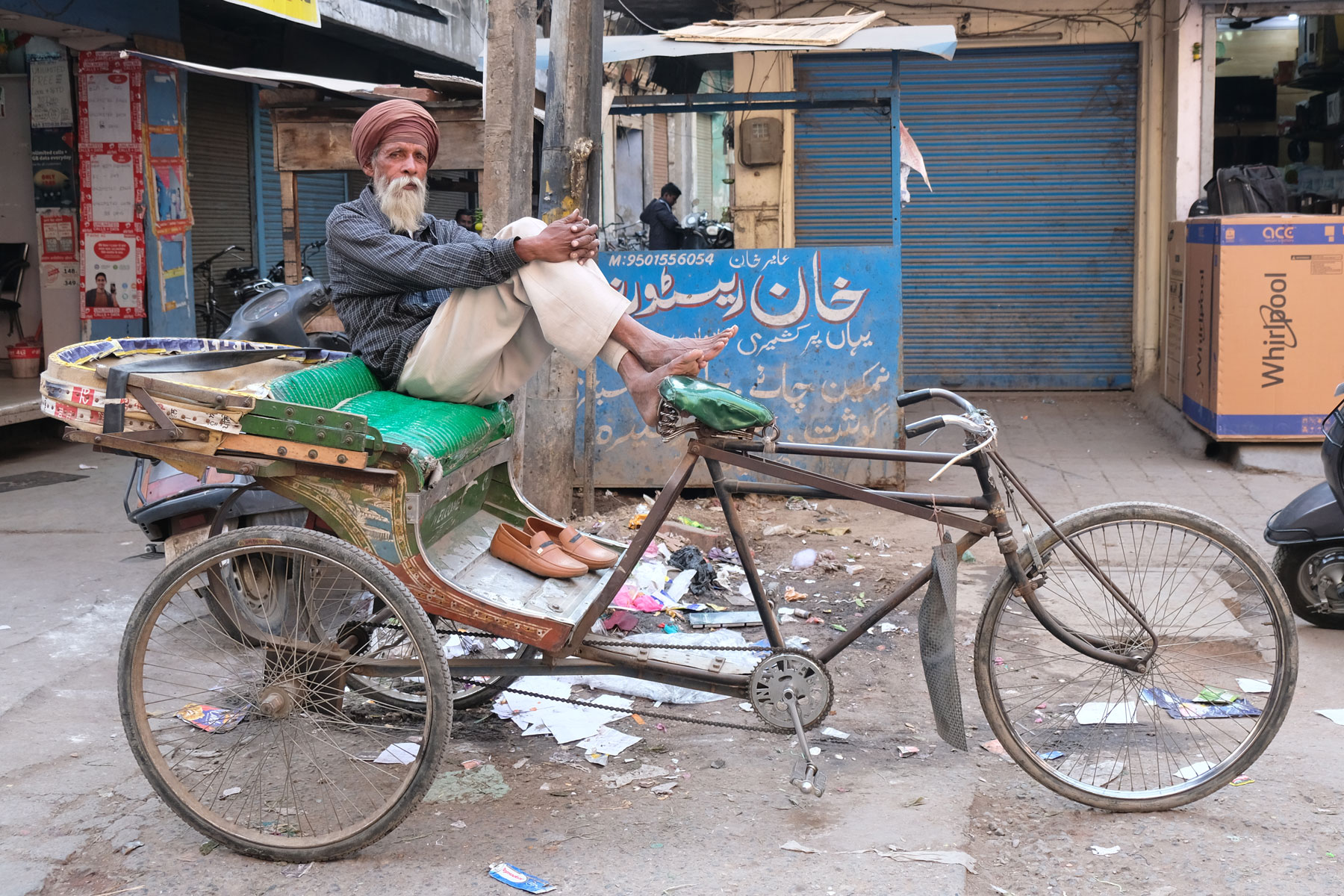 Ein indischer Mann sitzt auf einer Fahrradrikscha und stützt seine Füße auf dem Sattel ab.