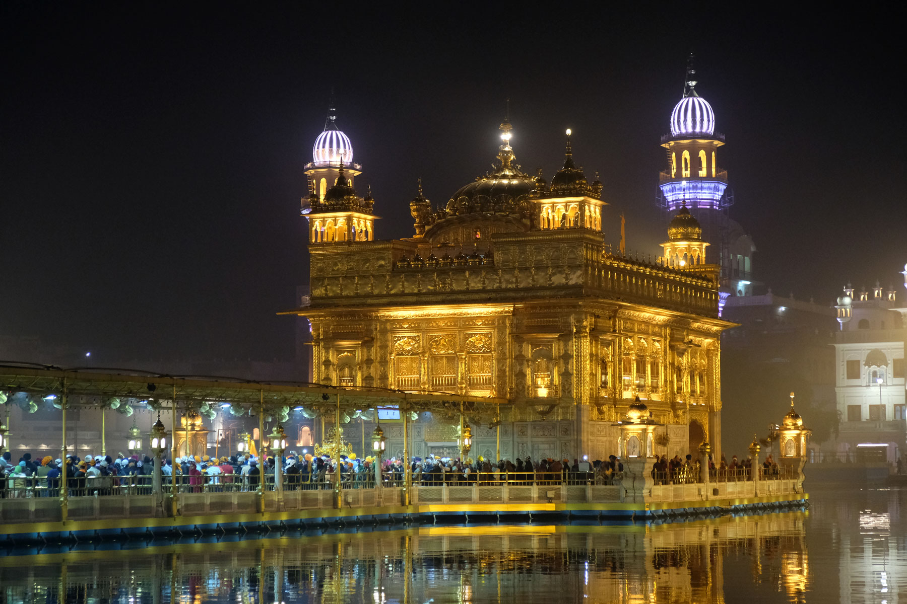 Pilger auf einem Steg vor dem goldenen Sikh-Tempel in Amritsar bei Nacht.