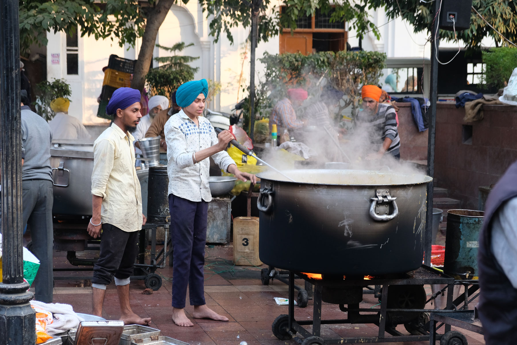 Zwei indischen Jungen stehen neben einem riesigen Kochtopf im Freien.