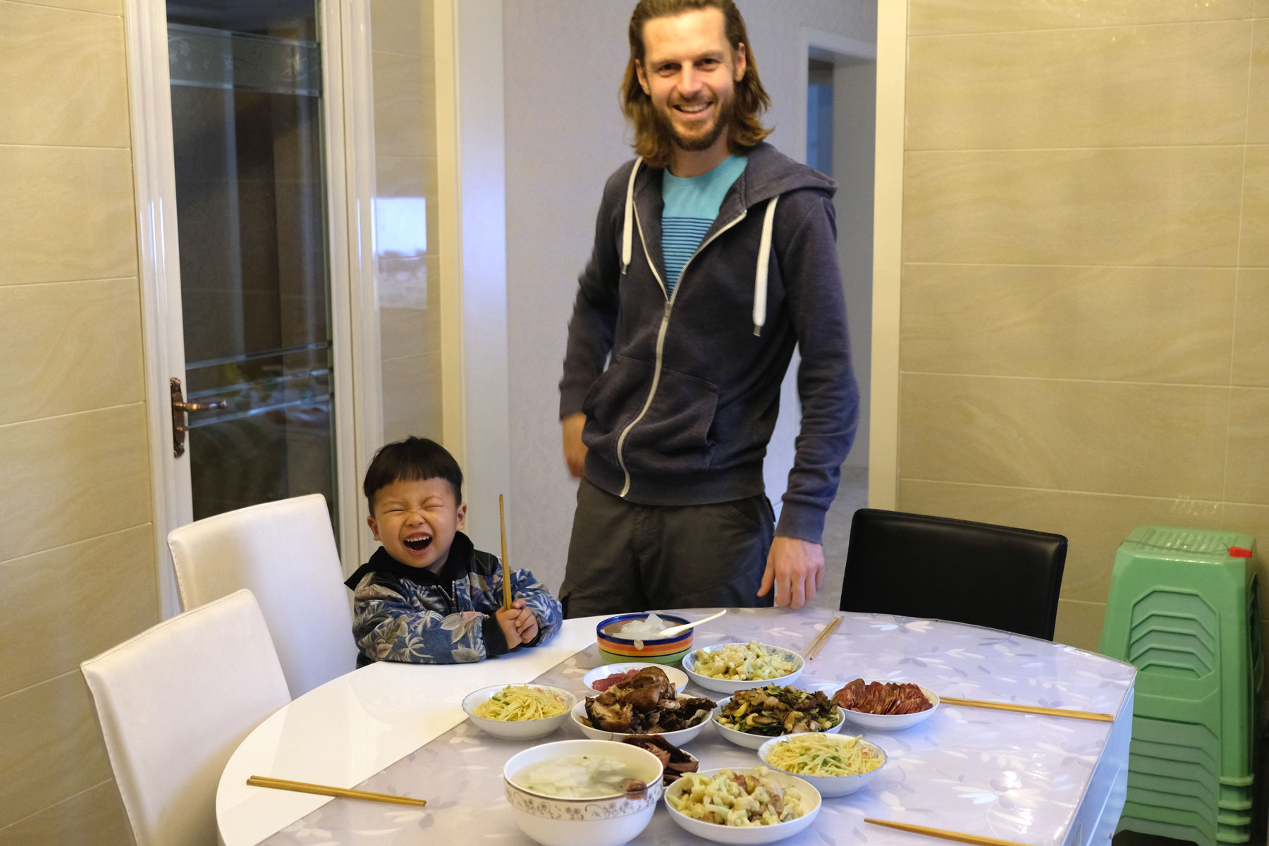 Leo steht neben einem lachenden chinesischen Jungen hinter einem gedeckten Tisch.