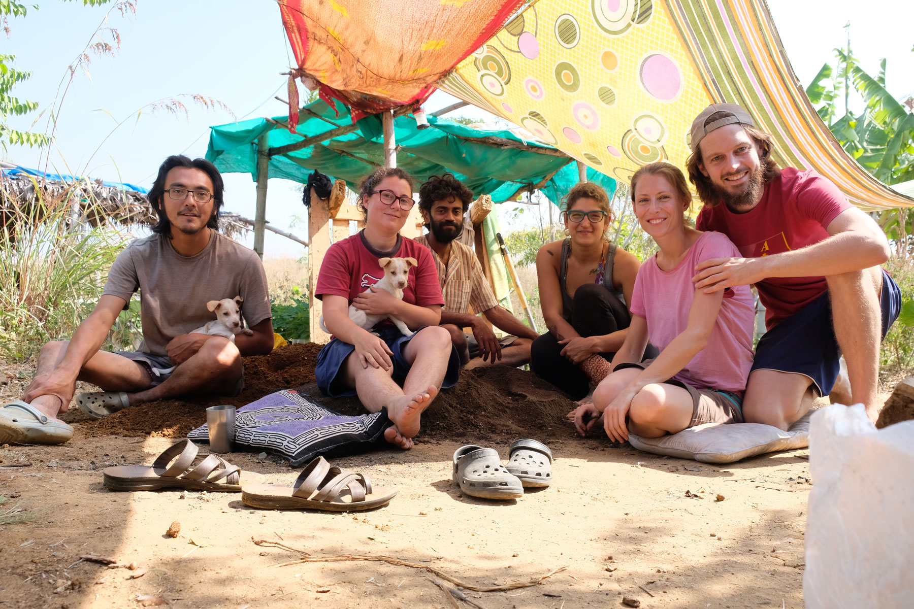 Leo und Sebastian sitzen mit Freiwilligen auf dem Boden einer Permakultur-Farm in Indien.