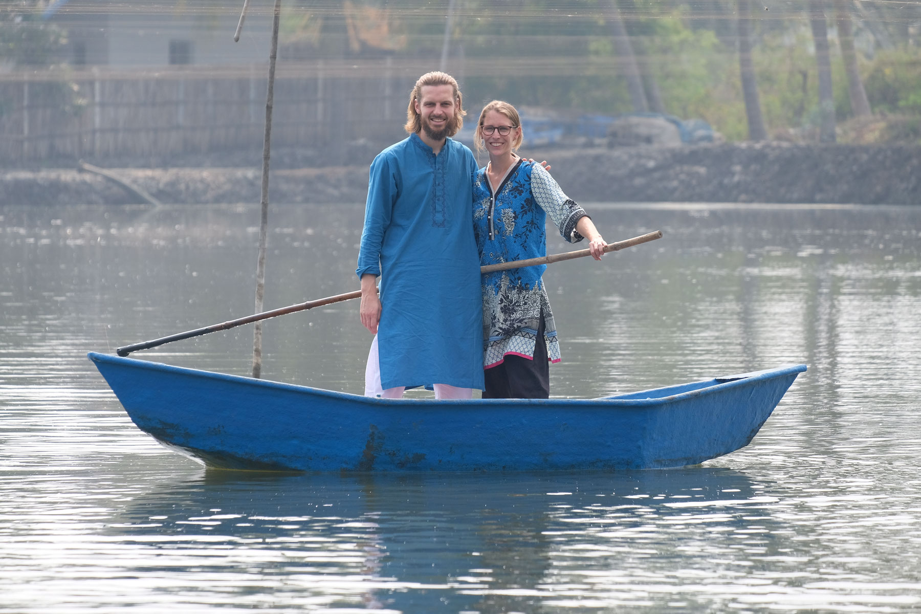 Sebastian und Leo stehen in einem kleinen Boot auf einem See und halten einen langen Stock in der Hand.