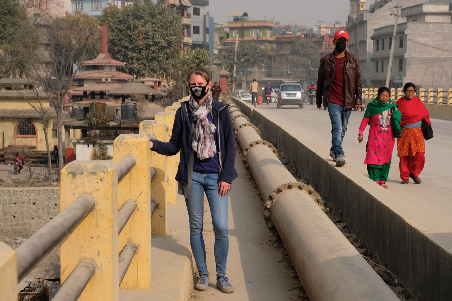 Leo steht auf einer Brücke in Kathmandu und trägt eine Atemschutzmaske.